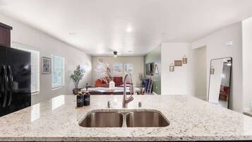 A kitchen with a granite countertop, stainless steel sink, and a refrigerator.