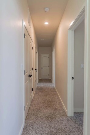 A narrow hallway with carpeted floors, white walls, and doors on both sides. - Stylish 4BR Escape  Open Layout  Smart TVs A (El Paso)