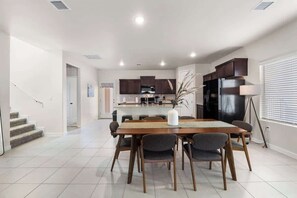 Une cuisine moderne avec des meubles de couleur sombre, un îlot central et un coin repas comprenant une table et des chaises en bois.