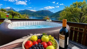 Ein Whirlpool mit einer Weinflasche und einer Obstschale auf einem Balkon mit Blick auf einen See und Berge.