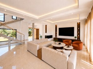 A modern living room with a sectional sofa, a flat-screen TV, and a staircase. - Palm Oasis Estate Dar Bouazza – 2 Private Villas • 16 Guests • 25m Swimming Pool (Tamaris)