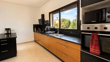 Una cocina moderna con encimera negra, armarios de madera, estufa de acero inoxidable y ventana con vistas al verdor.
