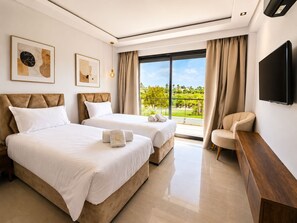Habitación de hotel con dos camas, televisión, escritorio y balcón con vistas.