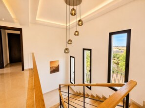 Un interior moderno con una escalera, vistas a través de amplios ventanales y una lámpara en el techo.