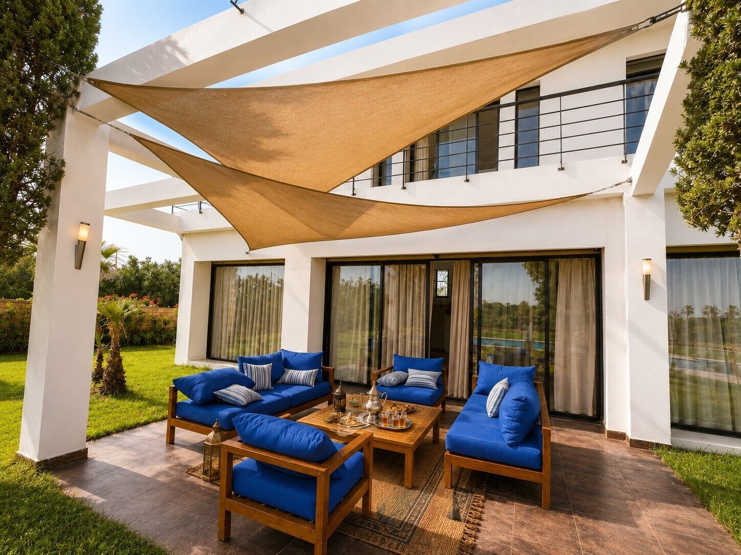 A modern outdoor seating area with sofas and a coffee table, surrounded by a white building with large windows and a shaded area.