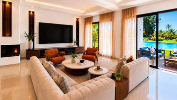 A modern living room with a flat-screen TV, comfortable seating, a fireplace, and a view of a swimming pool.