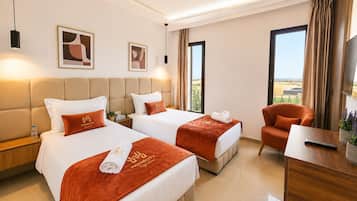 Quarto de hotel com duas camas, um sofá, uma televisão e vista para o exterior.