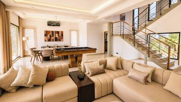 A modern living room with a pool table, a sofa set, and a staircase leading to an upper level.