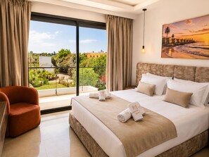A hotel room with a large bed, a chair, a painting of a sunset, and a view of greenery and buildings outside. - Palm Oasis Estate Dar Bouazza – 2 Private Villas • 16 Guests • 25m Swimming Pool (Tamaris)