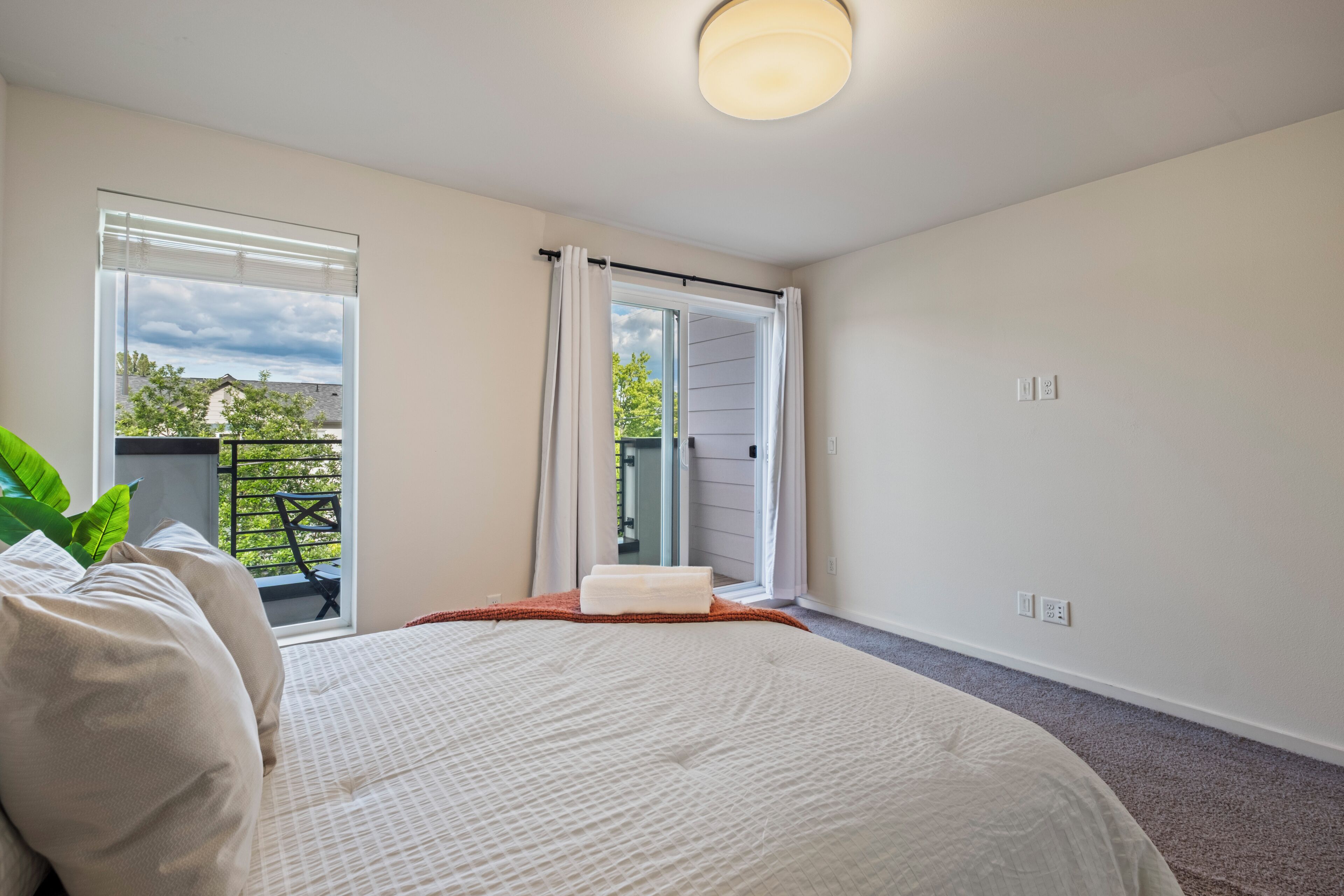 A bedroom with a bed, a window with curtains, a balcony, and a ceiling light.