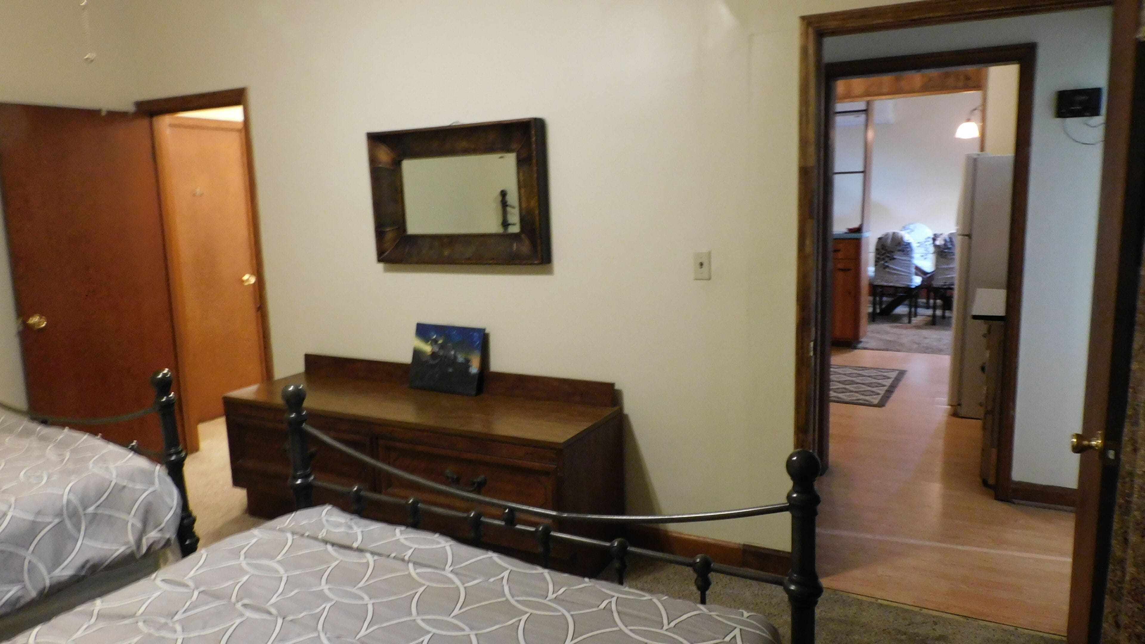 A bedroom with two beds, a dresser, a mirror, and a door leading to another room.