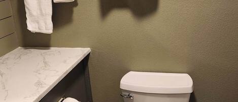 A bathroom with a toilet, a marble countertop, a towel rack with two towels, and a toilet paper holder.