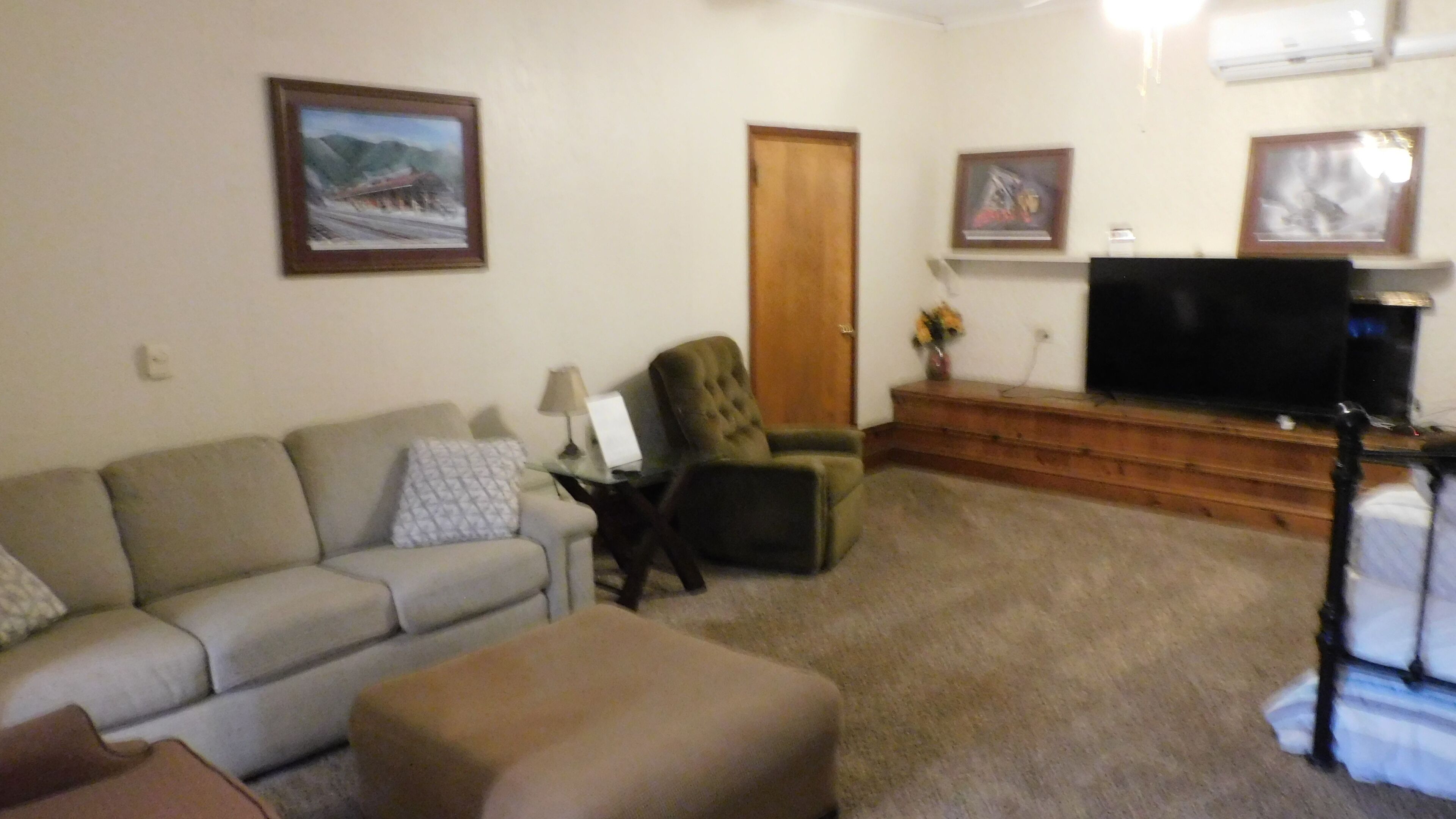 A living room with a sofa, an ottoman, a chair, a television, and framed pictures on the wall.
