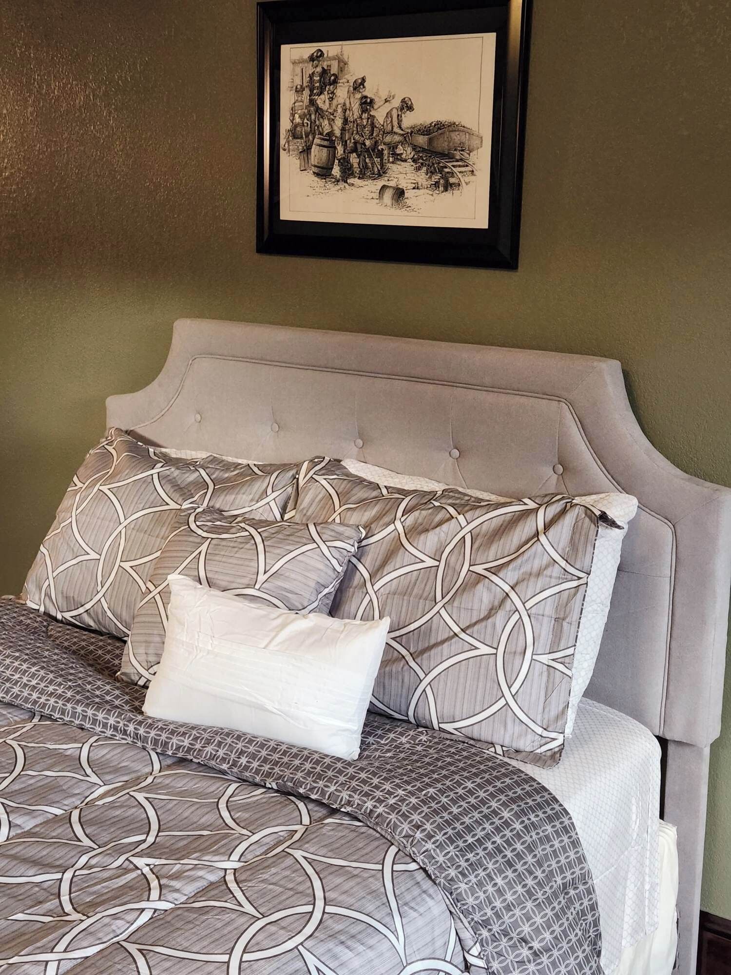 A neatly made bed with patterned bedding, a headboard, and a framed picture on the wall.