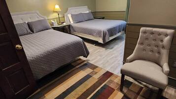 Habitación de hotel con dos camas, un ventilador de techo, una silla y una alfombra a rayas.