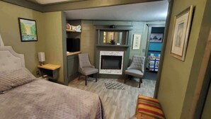 Un dormitorio con cama, una silla, chimenea y televisor.