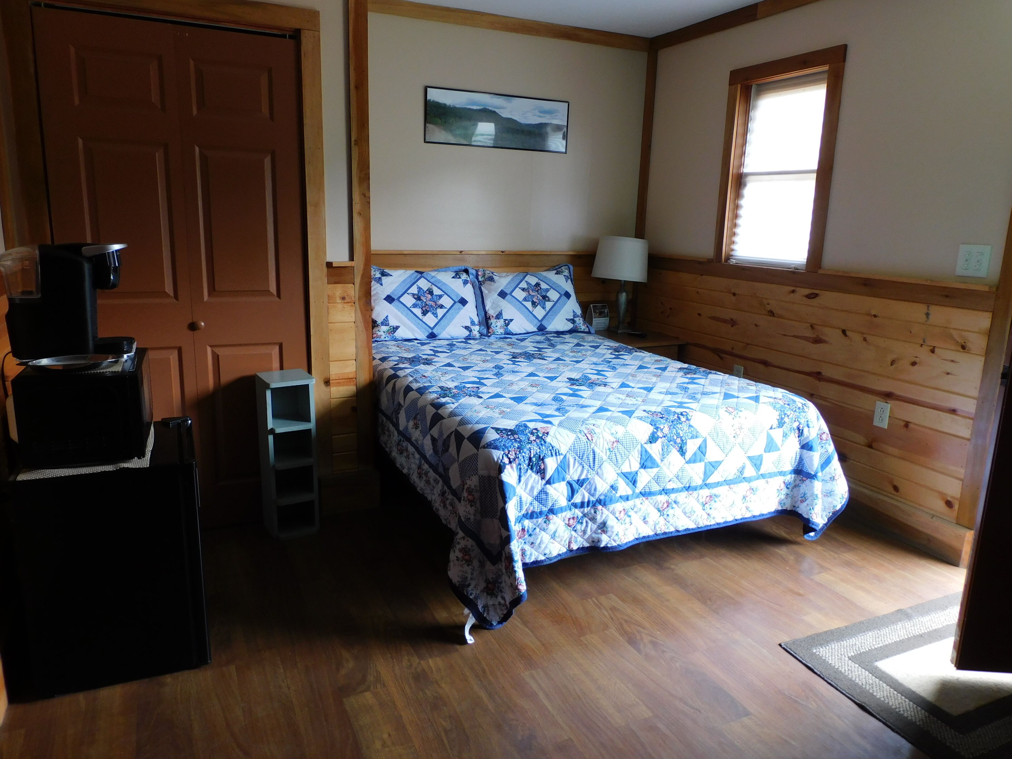 A bedroom with a bed, a desk, a chair, a lamp, and a window.