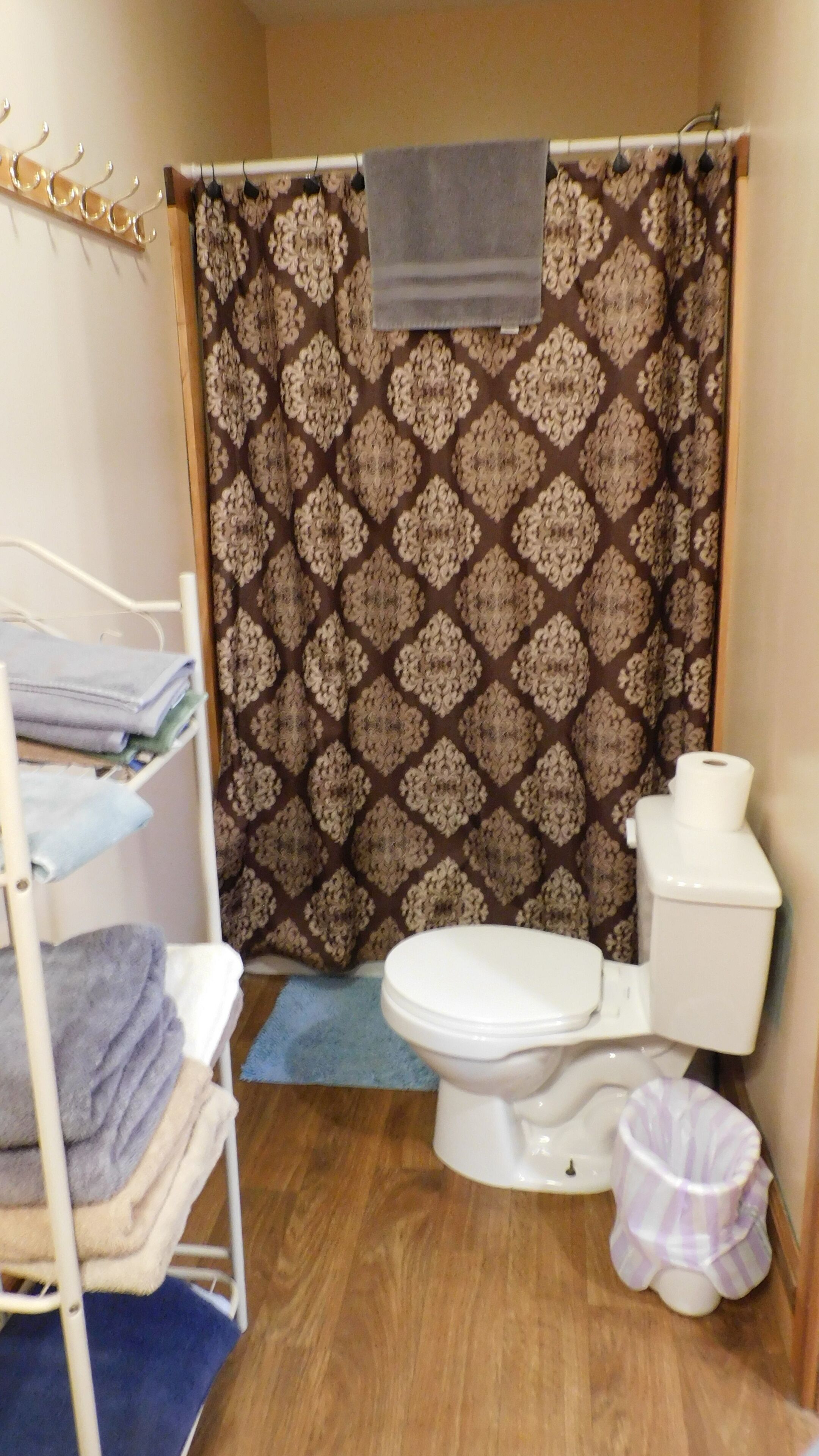 Un baño pequeño con cortina de ducha, inodoro, lavamanos y un estante metálico con toallas.