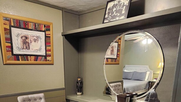 Una habitación con un sillón capitoné, un espejo, un cuadro enmarco y una chimenea.
