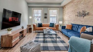 A living room with a TV, two sofas, a coffee table, and a brick wall. - Casa Hotels: Chic Industrial 2nd Floor Suite (Toronto)