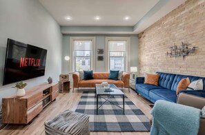 Ein Wohnzimmer mit Fernseher, zwei Sofas, einem Couchtisch und einer Ziegelwand.