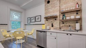 A modern kitchen with white cabinetry, a brick accent wall, and a dining area with yellow chairs. - Casa Hotels: Chic Industrial 2nd Floor Suite (Toronto)