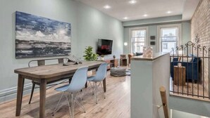 A modern living room with a wooden dining table, blue chairs, a large abstract painting, a flat-screen TV, and a staircase with a railing. - Casa Hotels: Chic Industrial 2nd Floor Suite (Toronto)