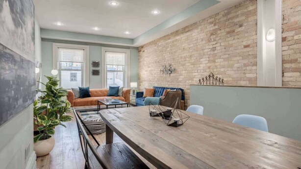 A modern living room with a brick wall, a wooden dining table, and a large window. - Casa Hotels: Chic Industrial 2nd Floor Suite (Toronto)
