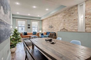 A modern living room with a brick wall, a wooden dining table, and a large window.