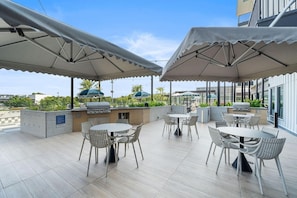 Eine Dachterrasse mit Sitzgelegenheiten im Freien, einem Grill und Sonnenschirmen.