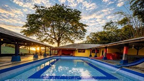 A swimming pool with a geometric tile pattern, surrounded by covered seating areas and a large tree.