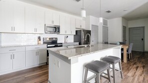 A modern kitchen with white cabinets, stainless steel appliances, a granite countertop, and a bar area with stools. - Landing | Spectacular 2BD, Clubhouse, Gym (Vestavia Hills)