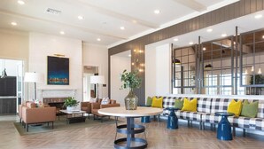 Eine geräumige Lobby mit einem runden Tisch, Sofas und einem karierten Sofa mit gelben Kissen.
