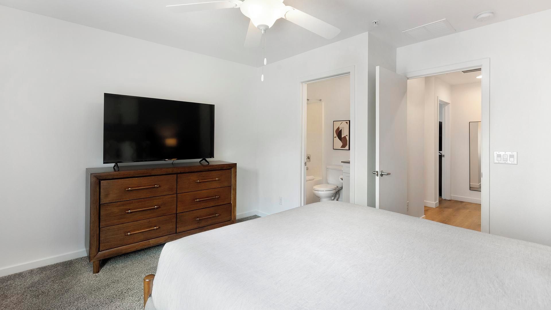 Ein Schlafzimmer mit einem Bett, einem Schminktisch, einem Fernseher und einem Deckenventilator.