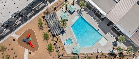 An aerial view of a residential complex with a swimming pool, a children's play area, and a covered patio.