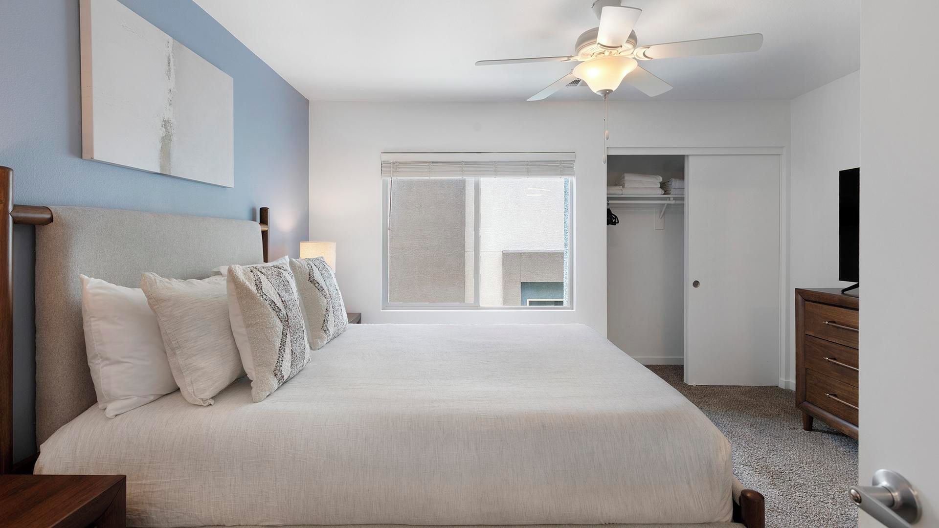 Une chambre à coucher comprenant un lit, un ventilateur de plafond, une armoire et un téléviseur.