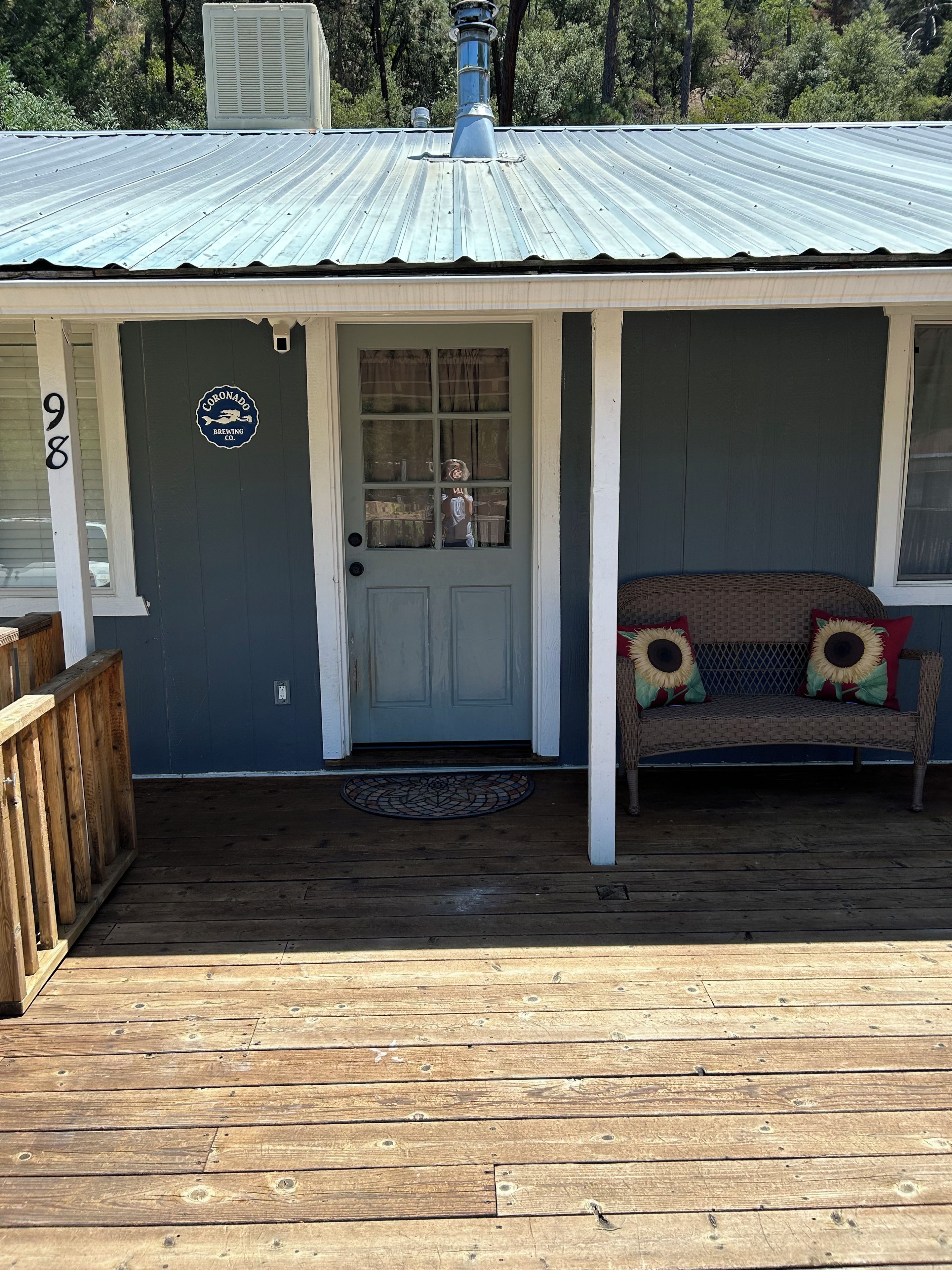 A building with a metal roof, a wooden deck, a door with a window, and a bench with sunflower cushions.