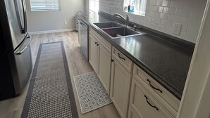 A kitchen with a refrigerator, sink, cabinets, and a window with blinds.
