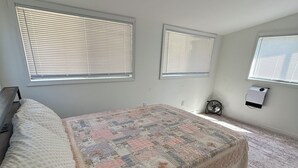 A bedroom with a bed, a bedside table, a heater, and a window with blinds.