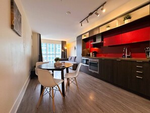 Une cuisine moderne avec des meubles de couleur sombre, un mur d’accent rouge et un coin repas comprenant une table ronde et des chaises.