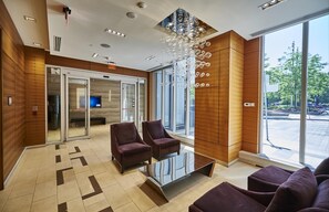 Un hall d’entrée moderne comprenant un comptoir d’accueil, deux fauteuils, une table basse en verre et de grandes fenêtres donnant sur l’extérieur.
