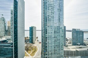 A high-rise building with a glass facade, surrounded by other modern buildings and a body of water in the background. - Suites Loft (Toronto)
