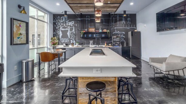 Una cocina moderna con una isla central, taburetes de bar, iluminación colgante y un ventanal grande.