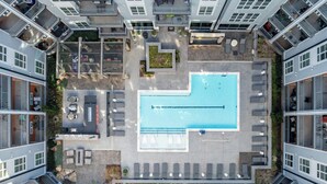 Vista aérea de un moderno complejo de apartamentos con piscina central, zonas de estar al aire libre y balcones.