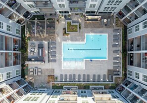 Ein Luftbild eines modernen Apartmentkomplexes mit einem zentralen Schwimmbad, Sitzgelegenheiten im Freien und Balkonen.