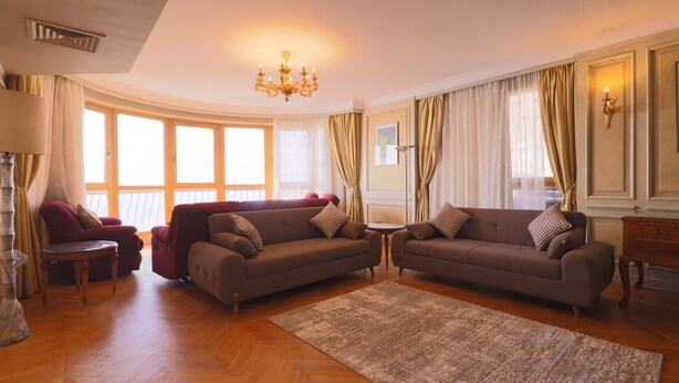 A spacious living room with two sofas, a chandelier, and large windows with curtains. - Nile front view & pyramids too.3 master BR+maid room.Large classy fully equipped (Cairo Governorate)