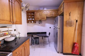 Eine kompakte Küche mit Holzschränken, einer schwarzen Arbeitsplatte, einem Kühlschrank, einer Spüle und einem Ventilator.