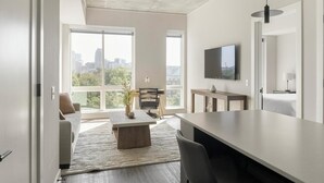 Een moderne woonkamer met uitzicht op de stad, een eethoek en een aan de muur bevestigde televisie.
