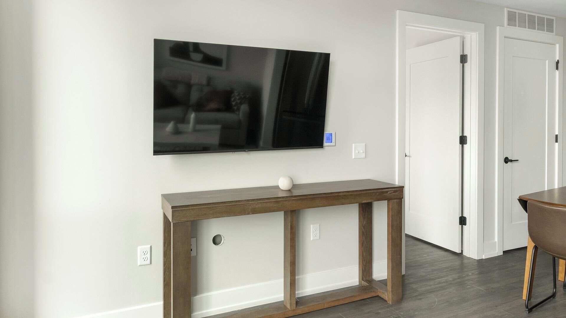 A living room with a flat-screen TV mounted on the wall, a wooden console table, and a door with a handle.