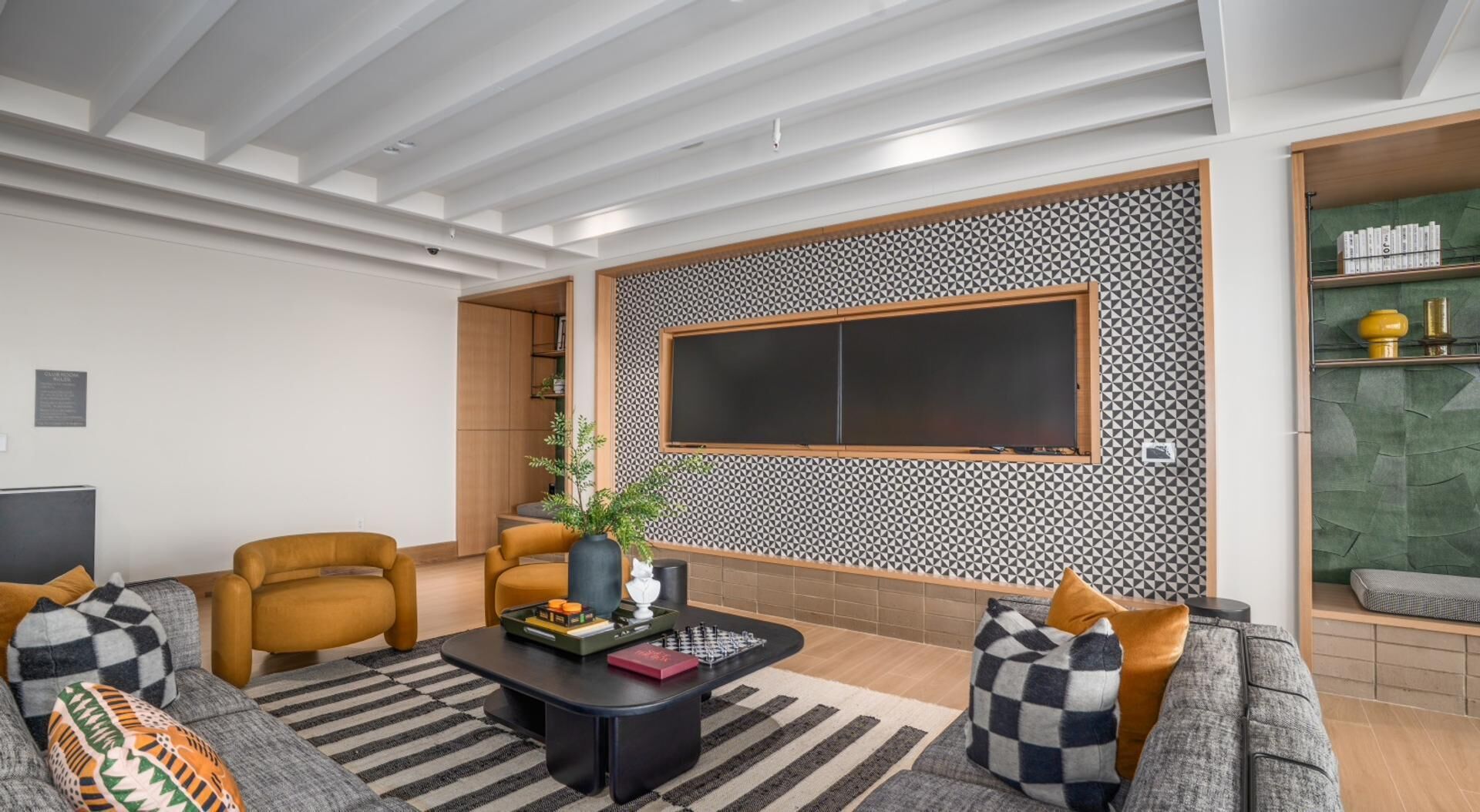 Een moderne woonkamer met een grote flatscreen-televisie, twee banken, een salontafel en een behang met patroon.